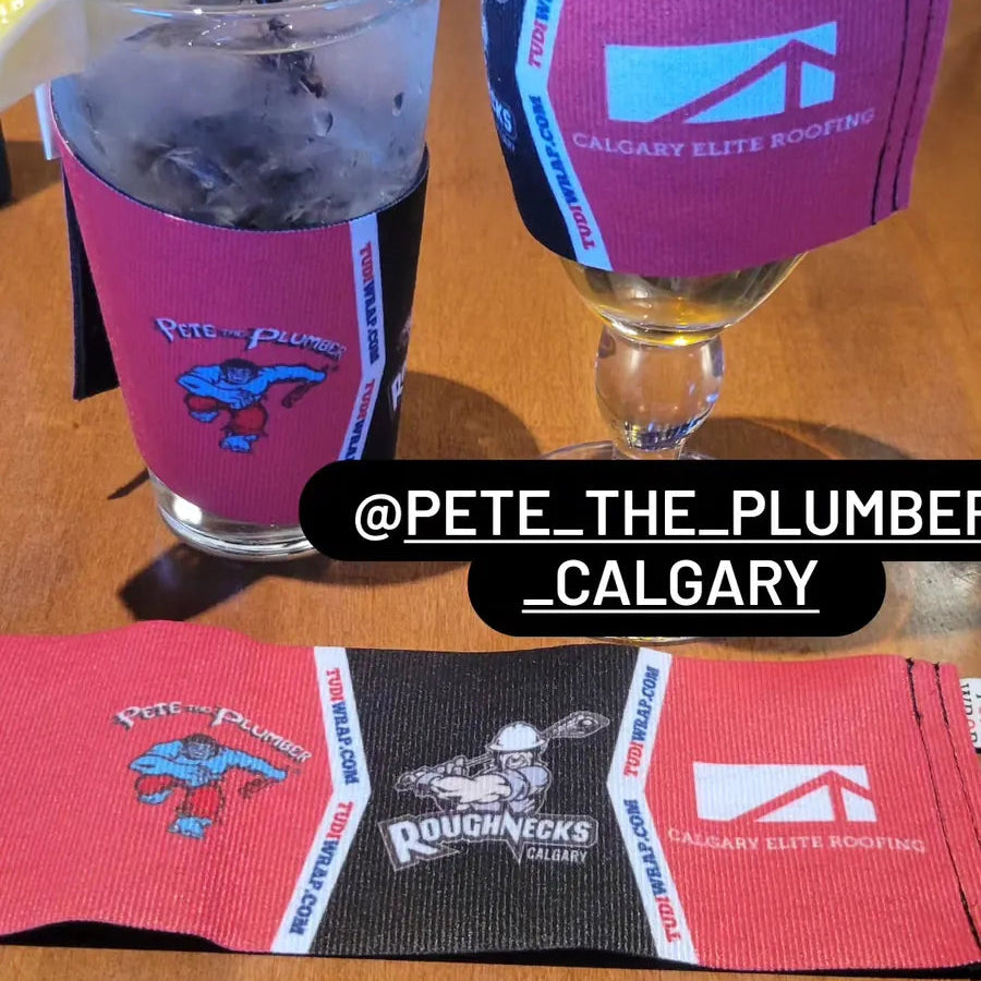 Two glasses with pink and black drink coasters featuring logos, on a wooden surface.